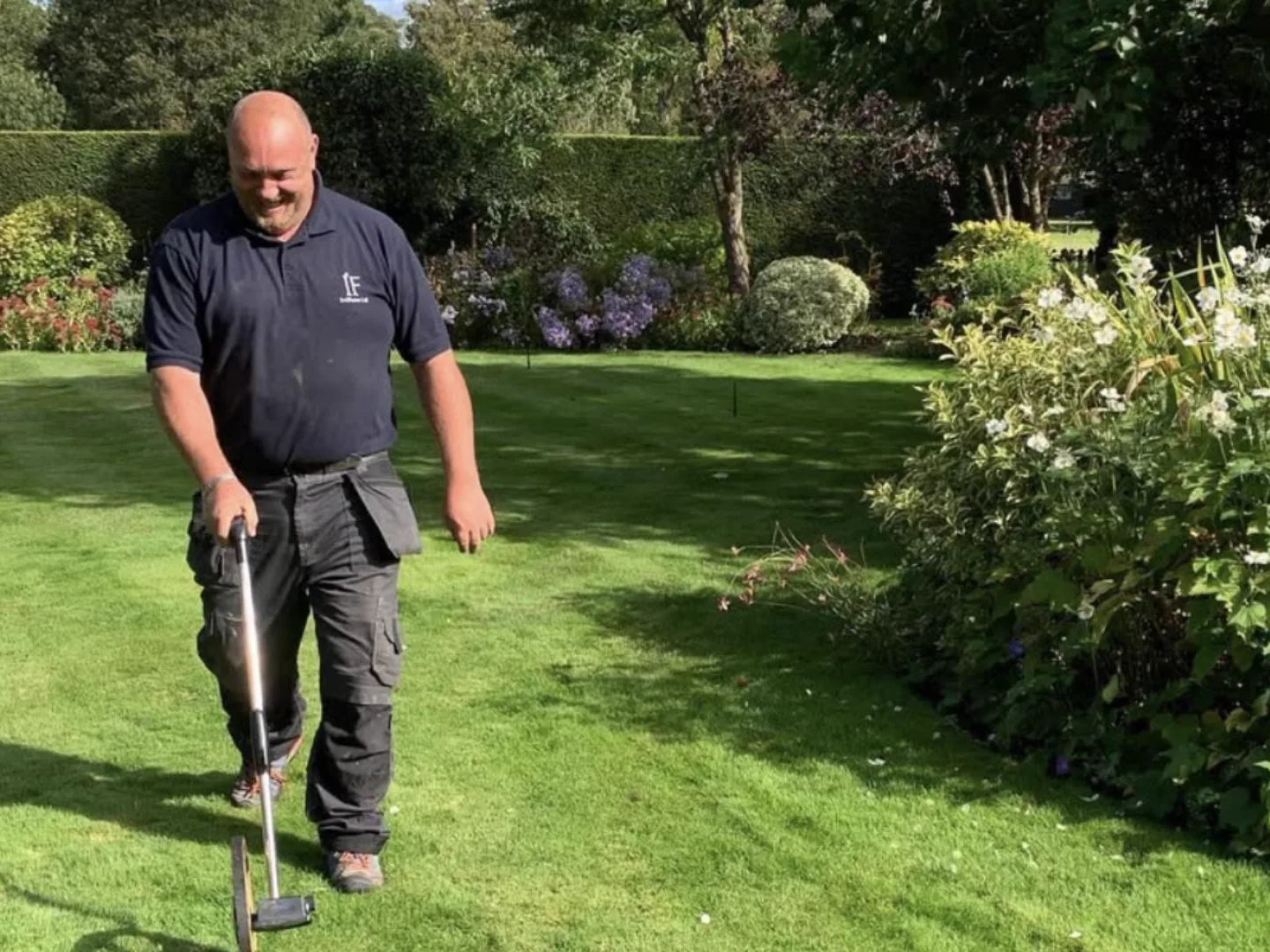 Engineer in a navy IrriFence polo pushing a measuring wheel across a lawn during a site survey