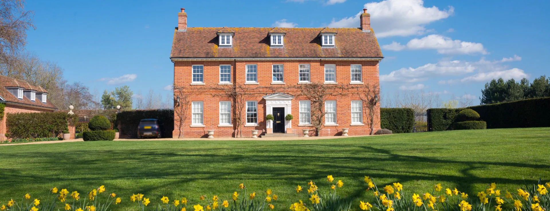 Red-brick house with a manicured lawn and a border of daffodils